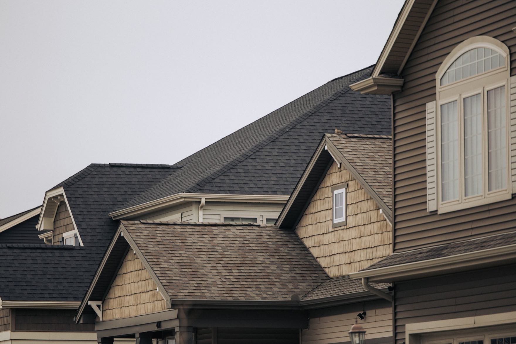 Pitched asphalt-shingle and cedar-shake rooflines on West Coast craftsman homes under an overcast Pacific Northwest sky